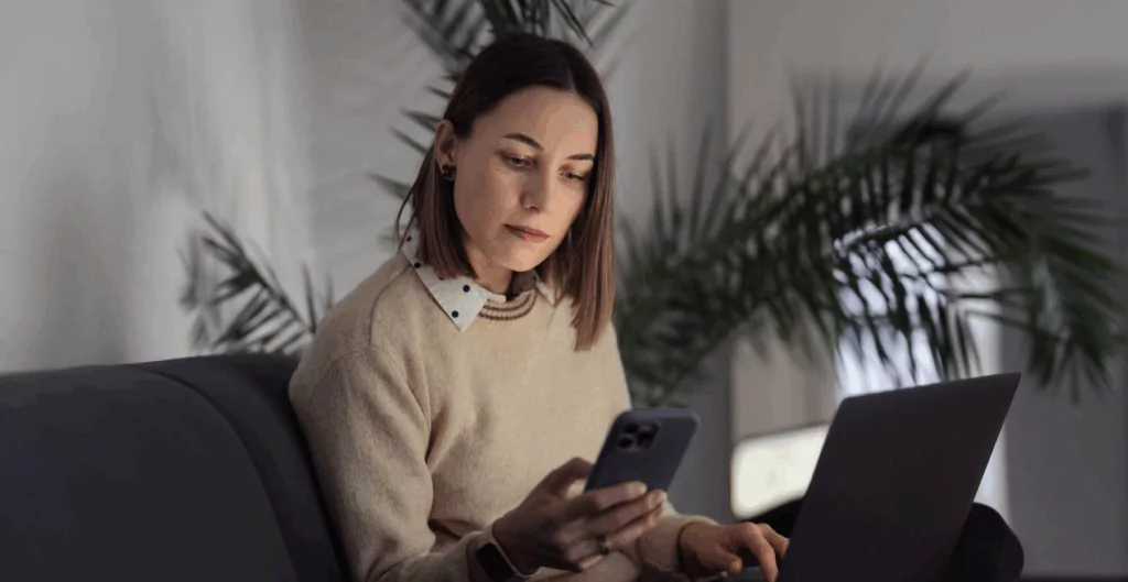 Mulher consultando smartphone e notebook, representando acesso digital ao consignado CLT.