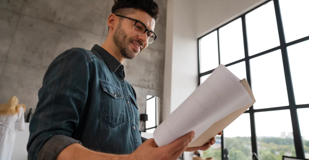 Homem sorrindo olhando para um papel com escritório brutalista ao fundo