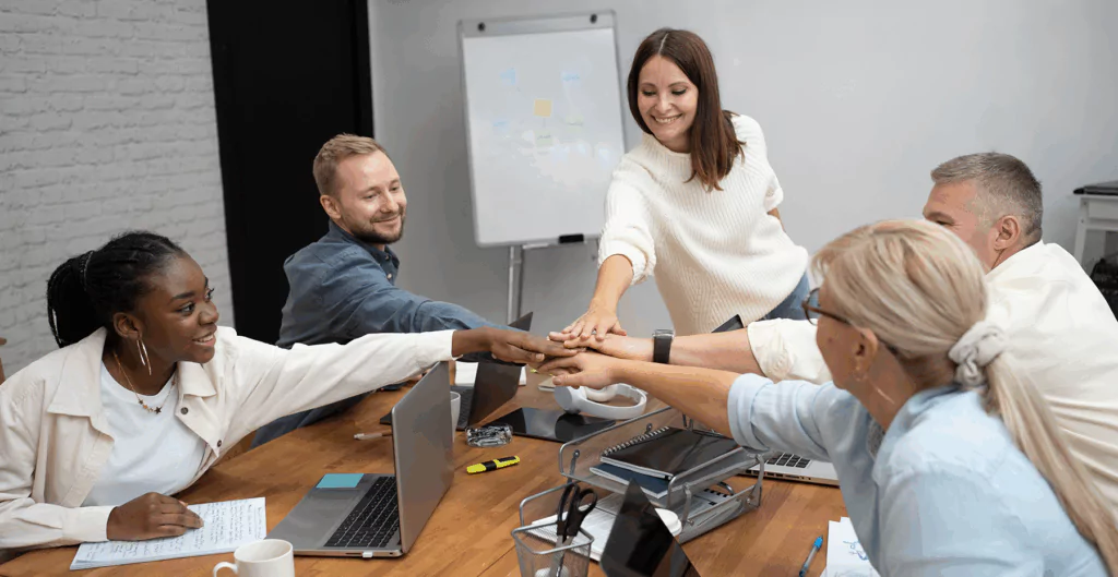 Equipe de trabalho em ambiente de reunião, as mãos juntas em símbolo de união e colaboração, representando trabalho em equipe e sucesso empresarial.