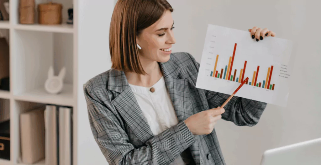 Mulher de cabelos lisos e sorriso apresentando gráfico de barras colorido em ambiente de escritório, mostrando crescimento empresarial.