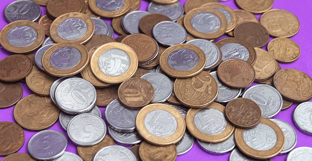 várias moedas de um real, cinquenta centavos e vinte e cinco centavos em fundo roxo