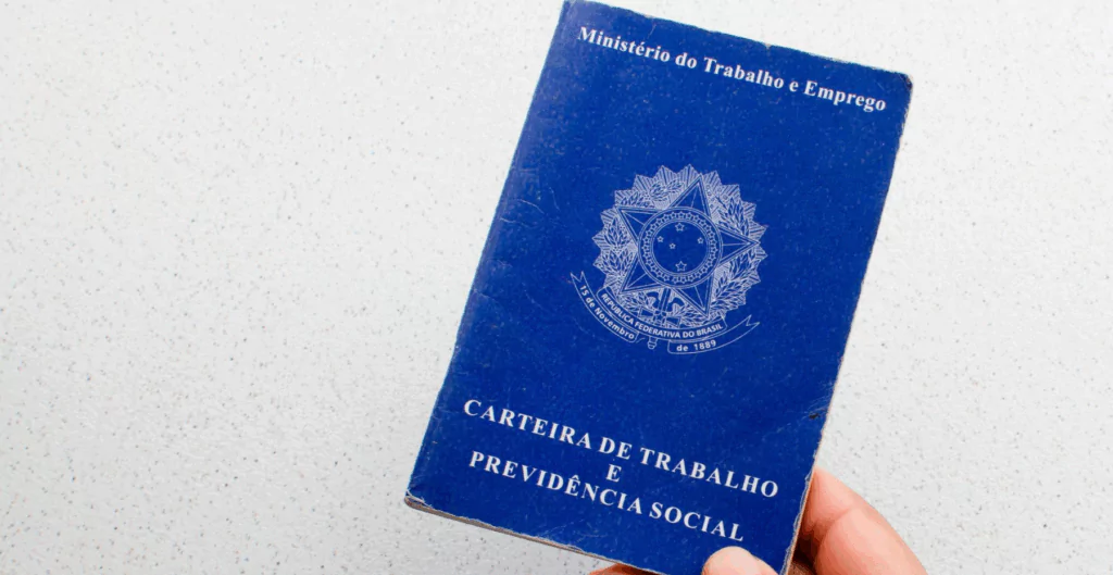 Pessoa segura carteira de trabalho em fundo branco sobre multas trabalhistas.