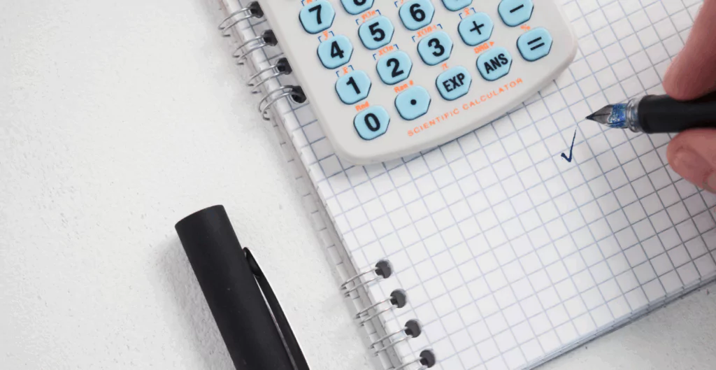Pessoa escreve em caderno com calculadora ao lado sobre multas trabalhistas.