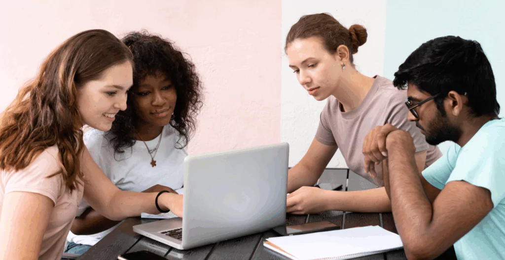 Quatro pessoas sentadas à mesa olhando para um notebook, jovens da geração nem nem
