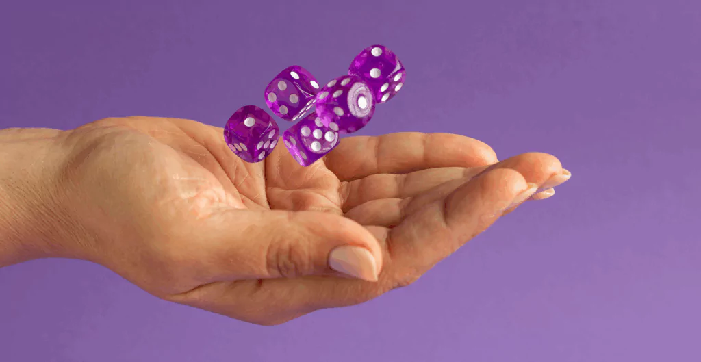 Mão segurando dados roxos com pontos brancos voando contra fundo roxo, destacando jogos de azar.