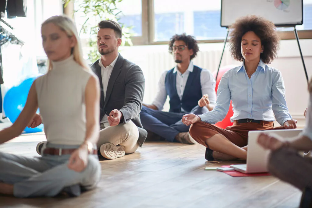 Grupo de pessoas praticando meditação em ambiente de escritório moderno, promovendo bem-estar e mindfulness no trabalho.