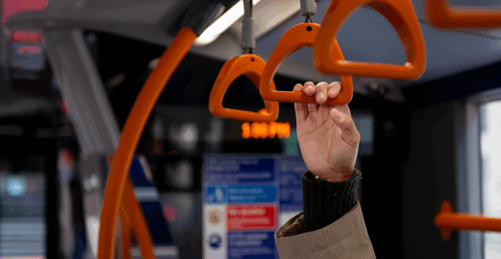 Pessoa segurando uma alça de transporte em um ônibus urbano, movimento cotidiano no transporte público de cidade brasileira.