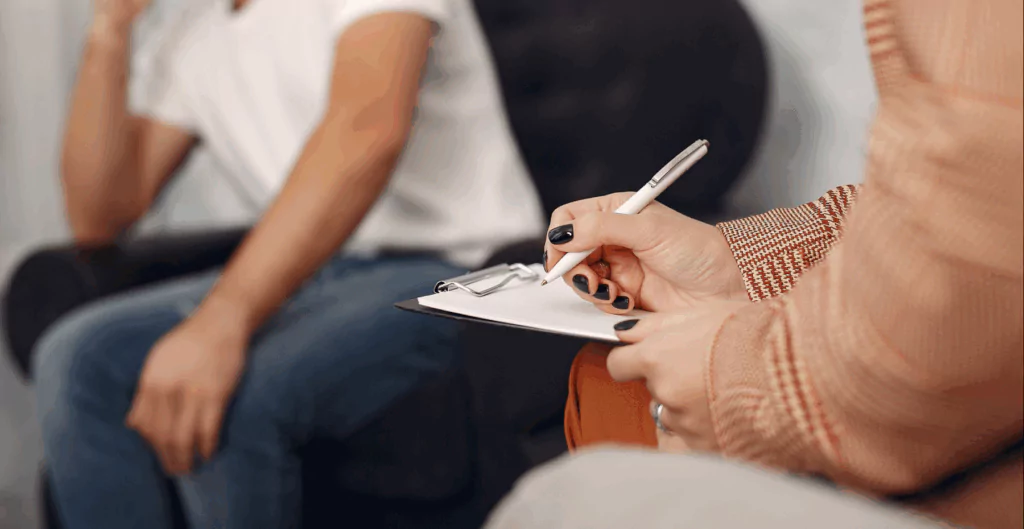 Profissional escrevendo em prancheta durante conversa, representando apoio psicológico e promoção da saúde mental no trabalho por meio de escuta e acompanhamento.