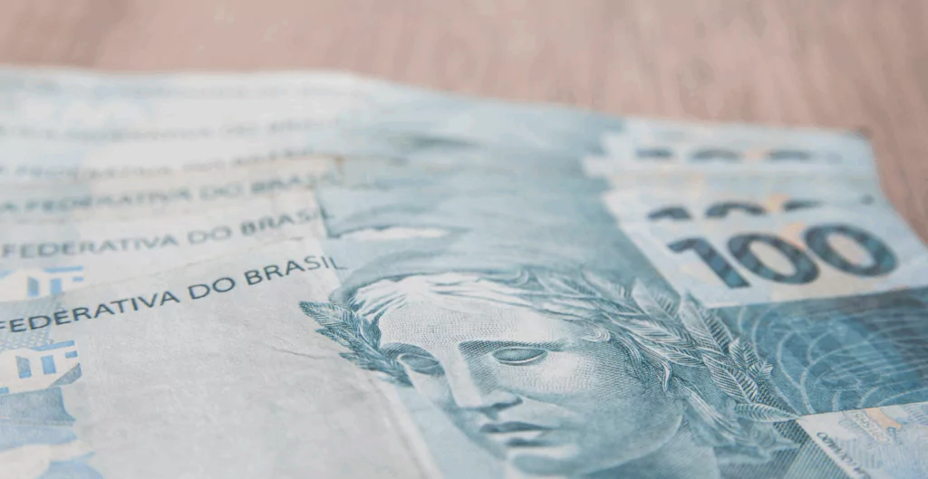 Detalhe de cédulas de cem reais, representando o crédito extra que o adiantamento depositante libera na conta.