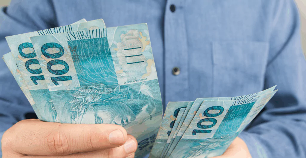 Pessoa segurando e contando notas de cem reais 