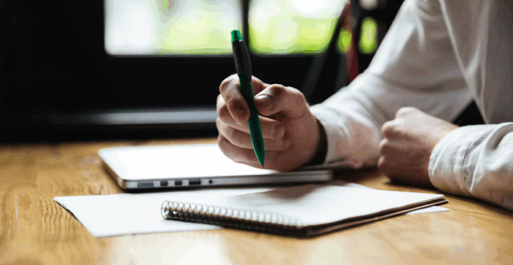 Pessoa escrevendo em caderno sobre uma mesa de madeira 