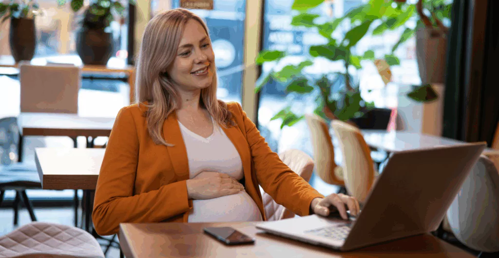 Mulher gravida sentada em cadeira mexendo em notebook 