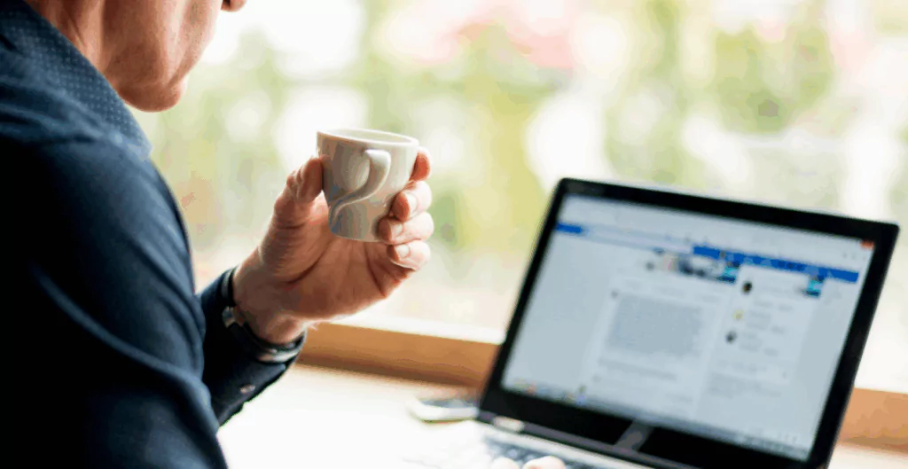 Homem tomando café enquanto utiliza seu notebook, aprendendo como usar o LinkedIn para networking profissional.
