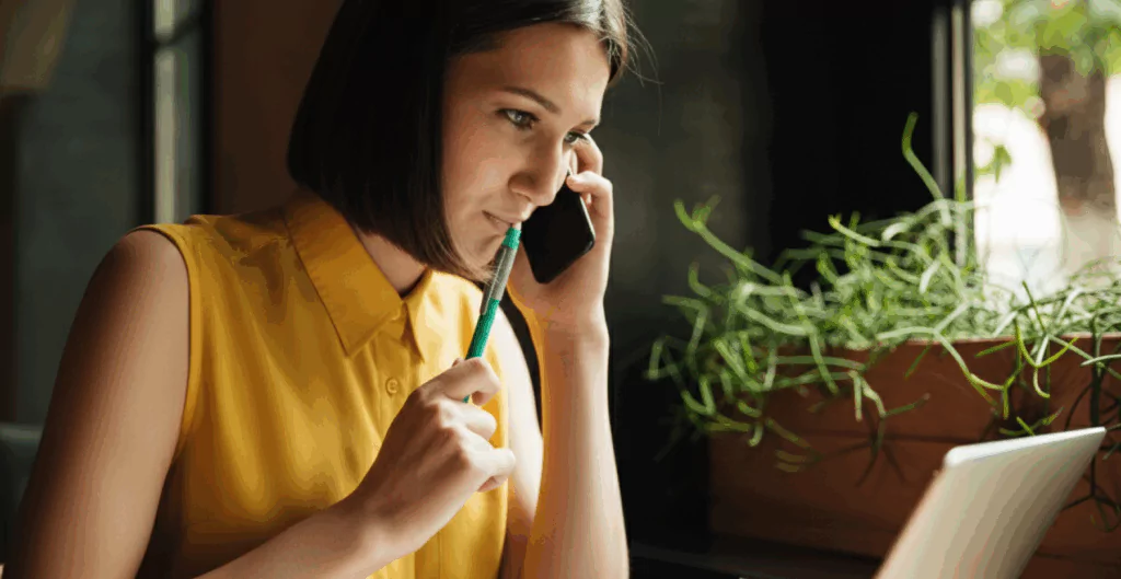 Mulher falando ao telefone com lápis na boca pensando 