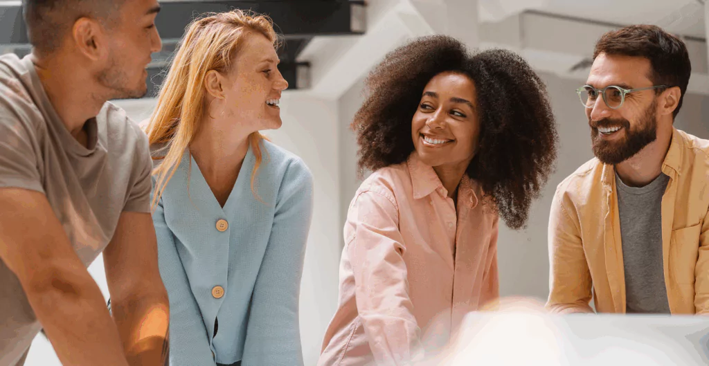 Grupo de pessoas sorrindo e conversando em ambiente de escritório, promovendo networking e conexão profissional.