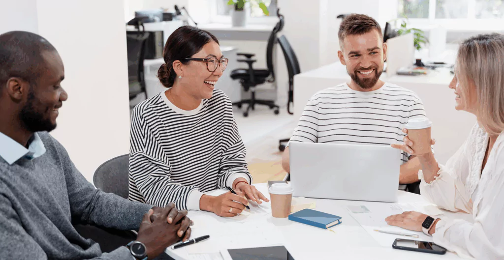 Quatro pessoas sorrindo ao redor de uma mesa em ambiente corporativo