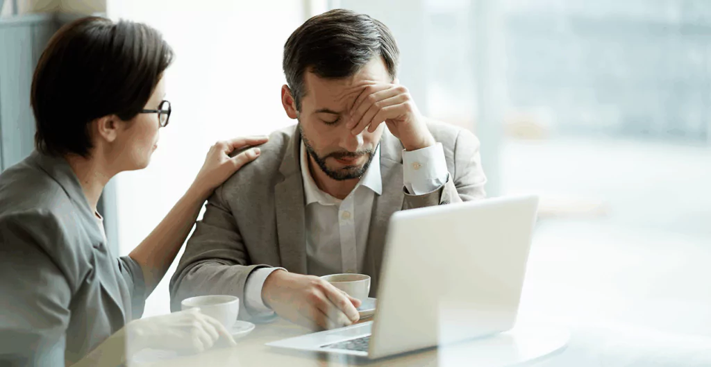  Colega de trabalho consolando homem estressado, que considera se pode trabalhar de atestado para cuidar da saúde mental.