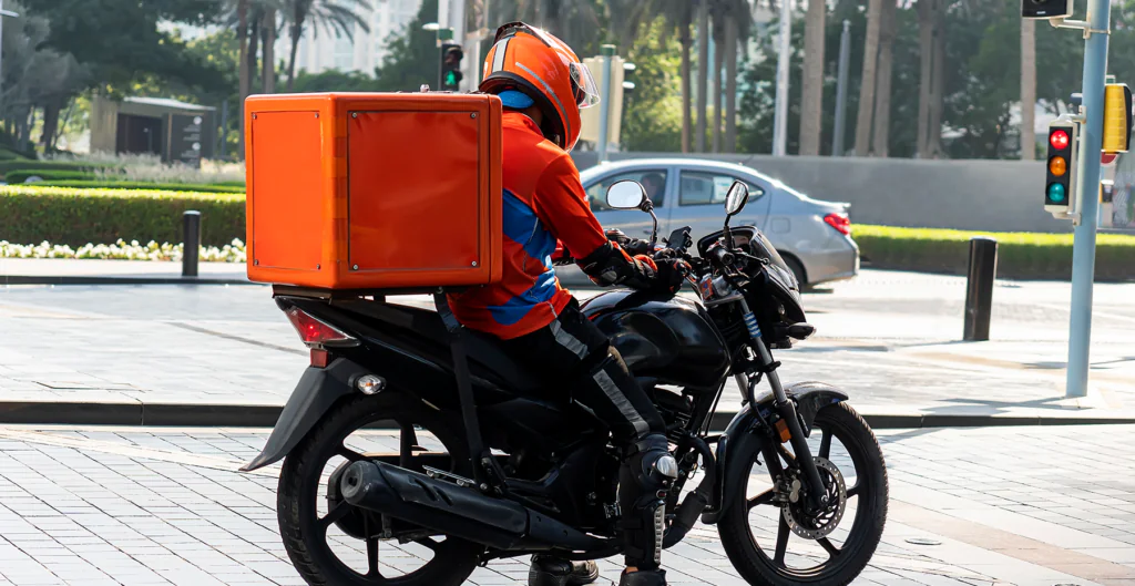 Entregador de pizza em motocicleta com compartimento térmico na cidade, realizando entrega de comida rápida com segurança e eficiência.
