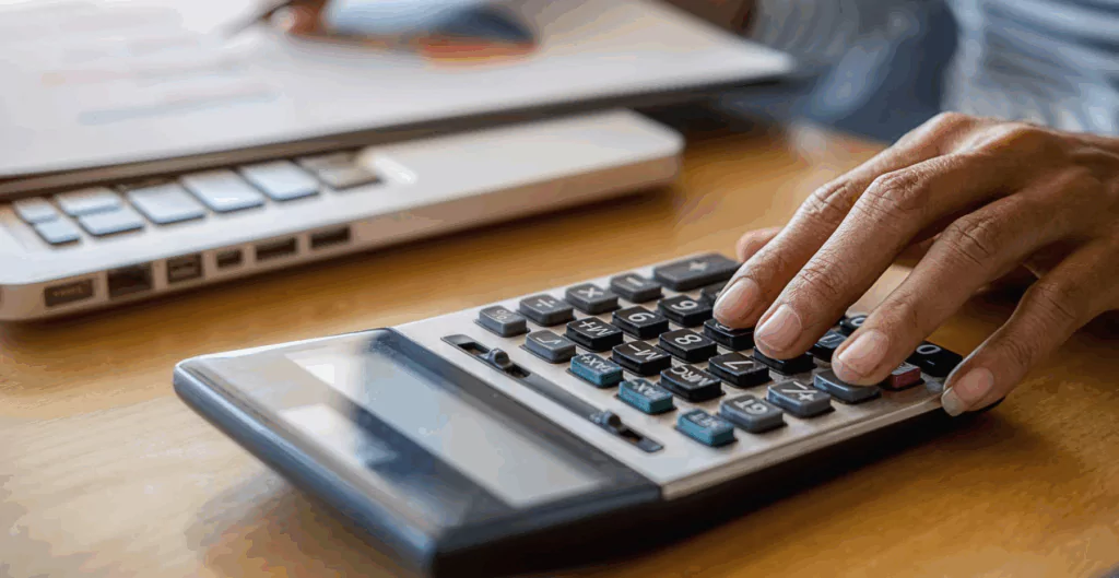 Pessoa usando uma calculadora em um ambiente de escritório, com teclado de computador ao fundo, destacando o uso de ferramentas de cálculo e análise financeira.