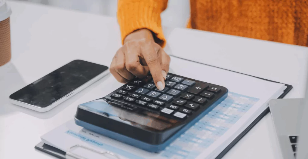 Pessoa ajustando uma calculadora em uma mesa de escritório com documentos e smartphone ao redor, símbolo de análise financeira ou contábil.