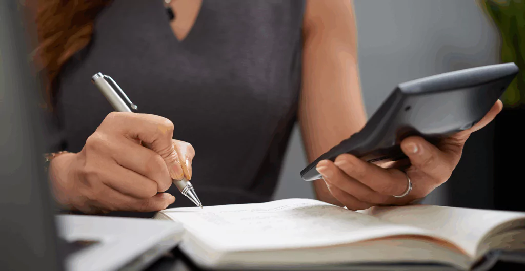 Mulher usando calculadora e fazendo anotação em bloco de notas.