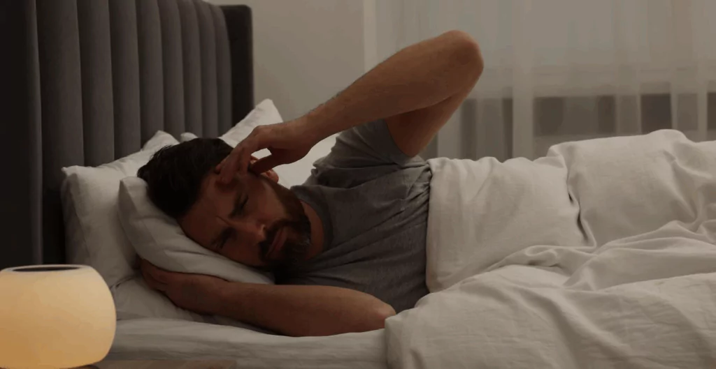 Homem deitado na cama com dificuldade para dormir e sinais de estresse, ilustrando sintomas de esgotamento mental