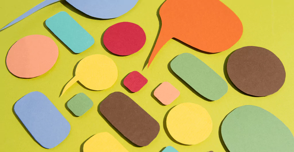 Diversas formas geométricas coloridas, incluindo círculos, retângulos e balões de fala, dispostas sobre uma superfície de cor amarela. Uma imagem vibrante que destaca cores variadas e formas diferentes para estimular criatividade e aprendizado visual.