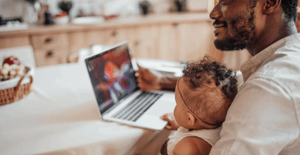 Homem sorridente segurando um bebê em um ambiente acolhedor e bem iluminado, transmitindo carinho e conexão familiar.