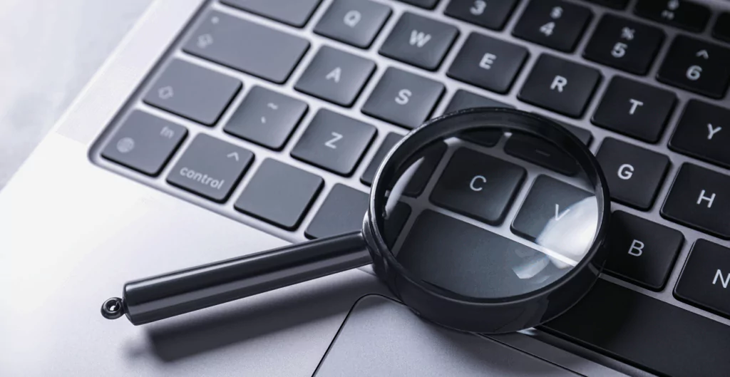 Lupa sobre teclado de notebook simbolizando a busca por dados e o monitoramento de cliques em sites e aplicativos.