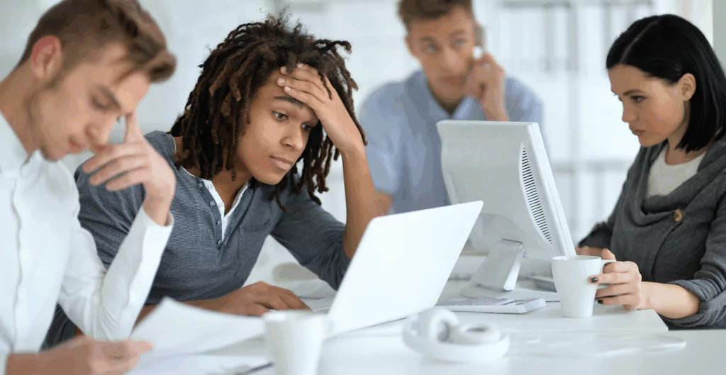 Equipe demonstrando cansaço e desmotivação, ilustrando os impactos negativos da neomania nas empresas e na produtividade.

