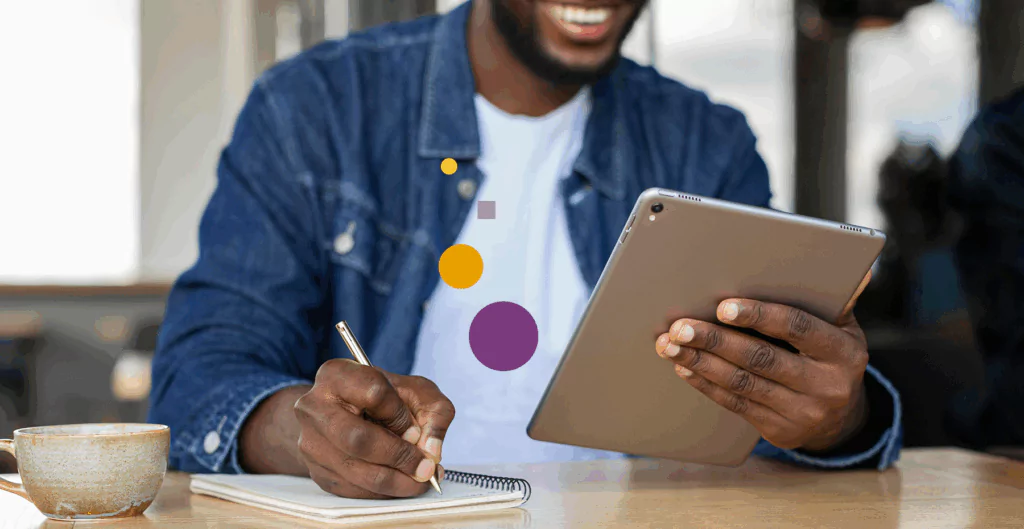 Homem sorridente usando tablet e fazendo anotações, promovendo a palavra-chave 'tecnologia' com ambiente de trabalho descontraído.