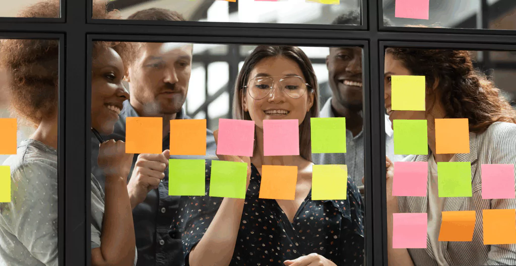 Grupo de profissionais em uma reunião de brainstorming com post-its coloridos na parede, promovendo criatividade e colaboração no ambiente de trabalho.