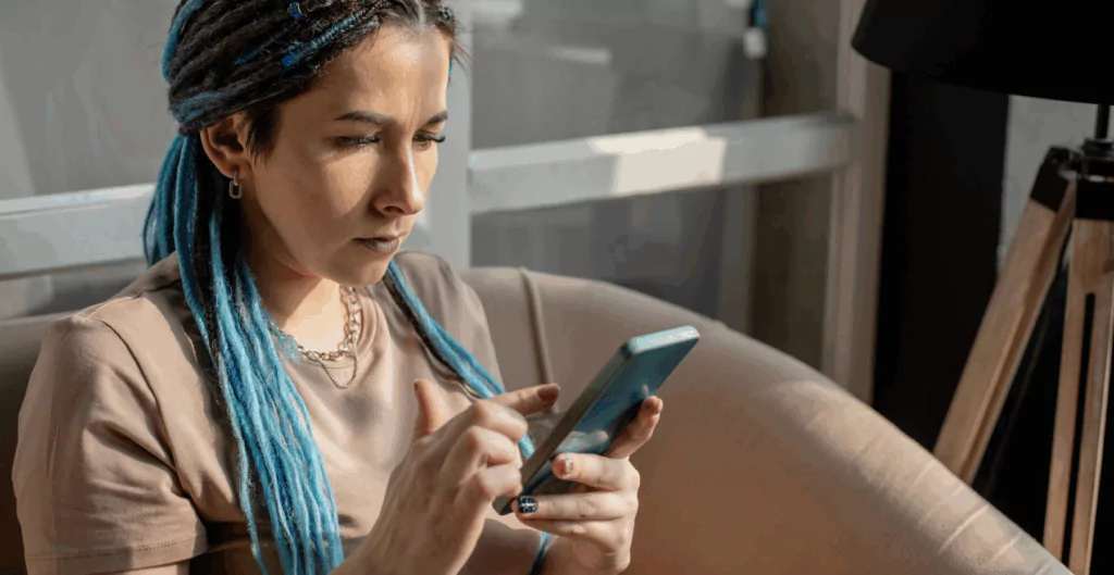 Mulher com tranças azuis sentada em sofá olhando um celular 