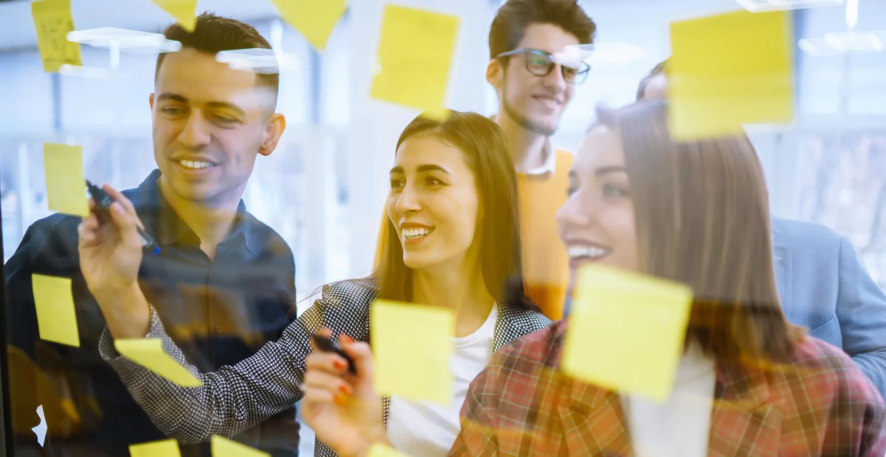 Equipe de profissionais colaborando e planejando projetos em uma reunião com post-its na parede, promovendo criatividade e inovação no ambiente de trabalho.