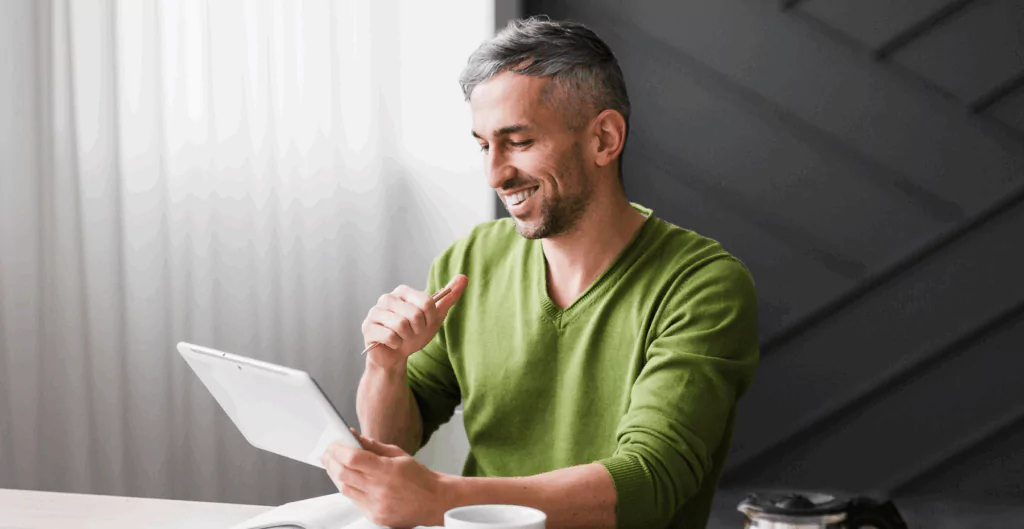 Homem feliz usando tablet em ambiente moderno com decoração minimalista, promovendo bem-estar na rotina diária.