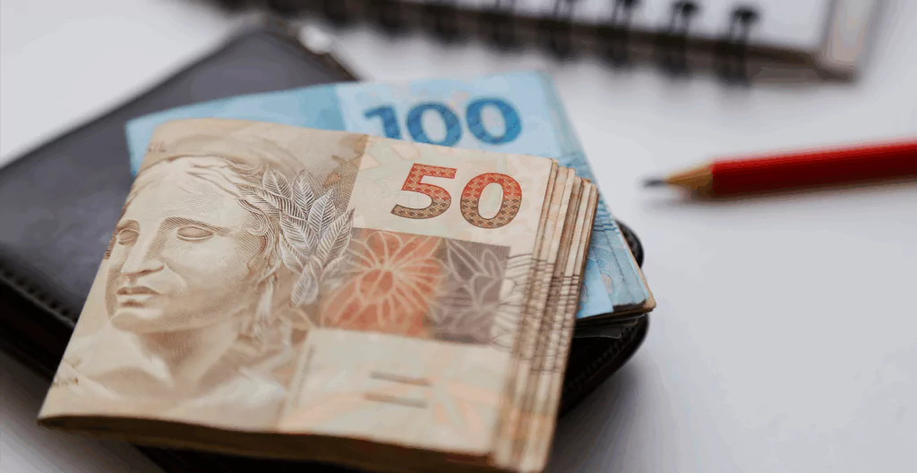 Dois maços de reais, sendo um de cinquenta e outro de cem, sobre uma mesa 