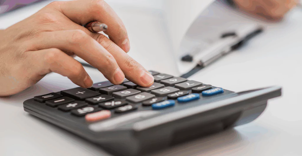 Pessoa usando uma calculadora, possivelmente realizando cálculos financeiros ou explicações de matemática, com foco na mão ativando os botões.