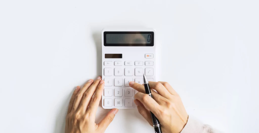 Mãos operando uma calculadora branca e segurando uma caneta sobre uma superfície clara