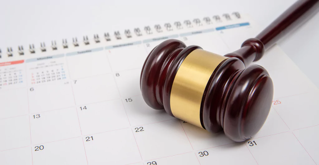 Martelo de juiz de madeira repousando sobre um calendário de mesa com números visíveis.