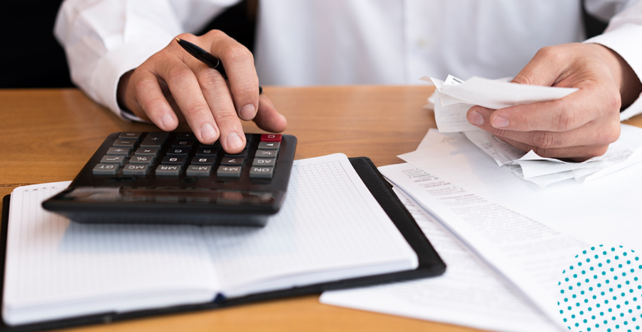 imagem de um homem sentado mexendo em uma calculadora e segurando folhas de papel