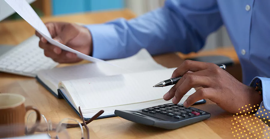 imagem de um homem sentado usando uma calculadora e segurando uma caneta e um papel