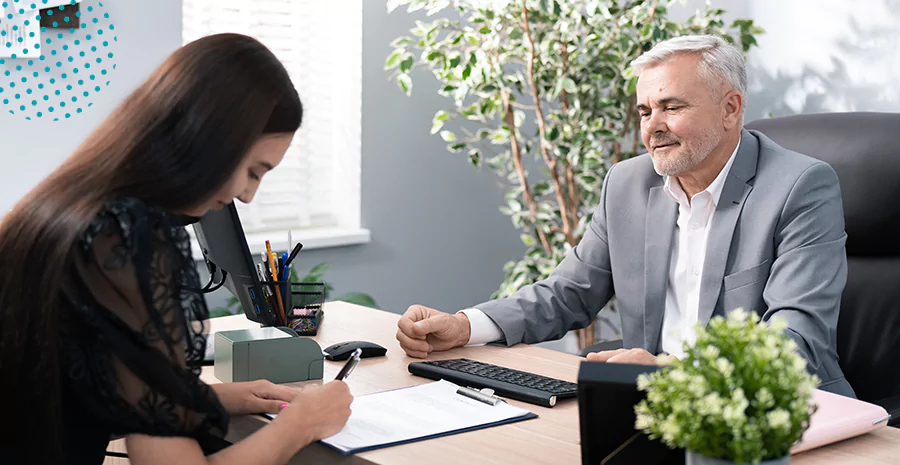 imagem de um homem e uma mulher em um escritório sentados, e a mulher assinando o contrato de experiência