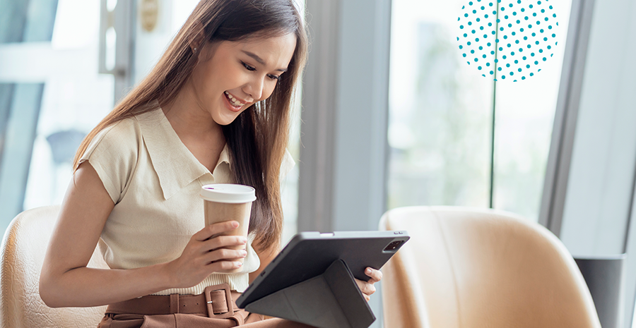 imagem de uma mulher sorrido segurando um copo com café e mexendo em um tablet