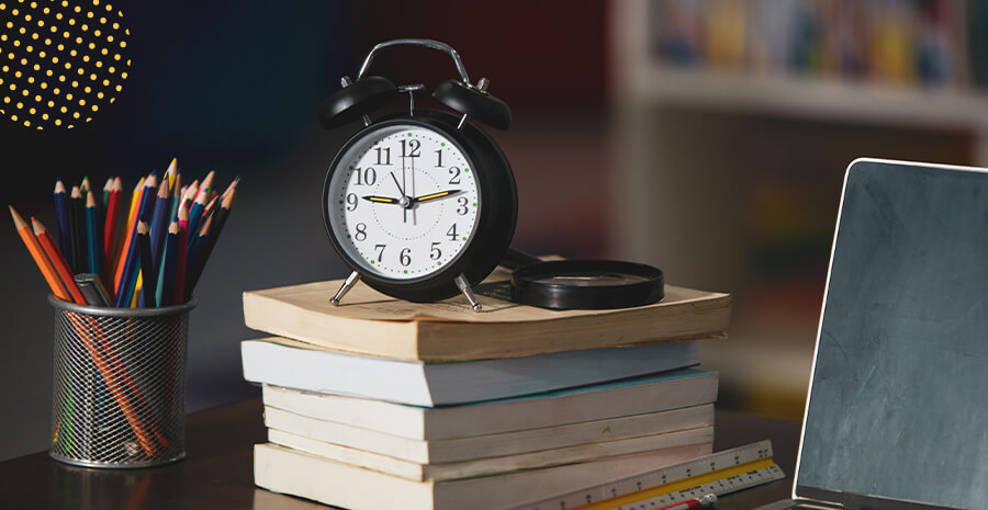 imagem de um relógio despertador em cima de livros sob uma mesa de trabalho