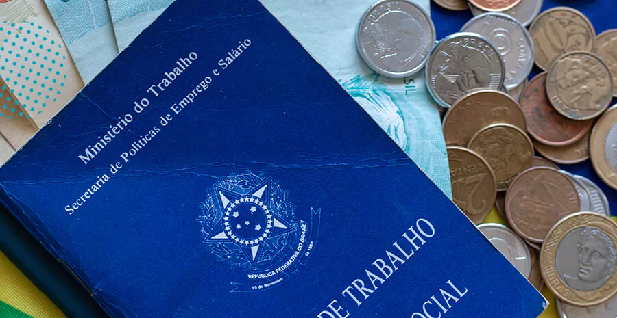 imagem de uma carteira de trabalho brasileira com moedas ao lado