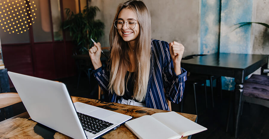 imagem de uma mulher com um semblante feliz comemorando em frente ao computador