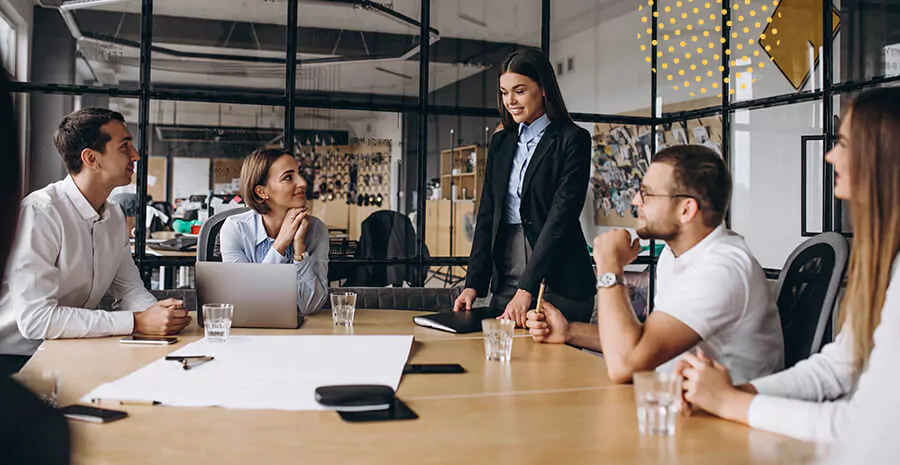 imagem de pessoas reunidas em uma mesa de trabalho com uma mulher em pé