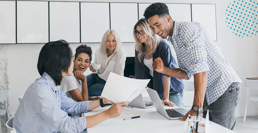 imagem de 5 pessoas diferentes em volta de uma mesa, duas sentadas e três em pé conversando