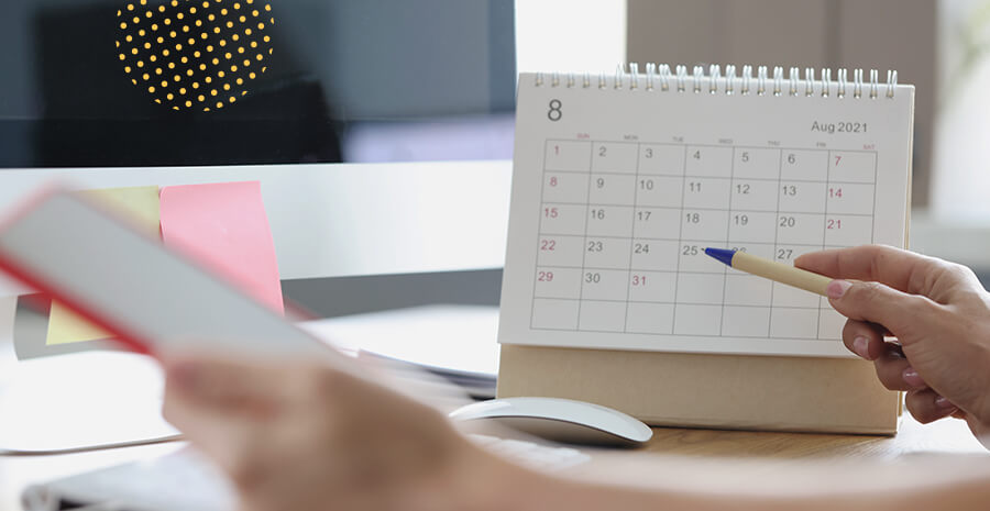 imagem de um calendário em cima de uma mesa com uma pessoa segurando uma caneta na frente dele