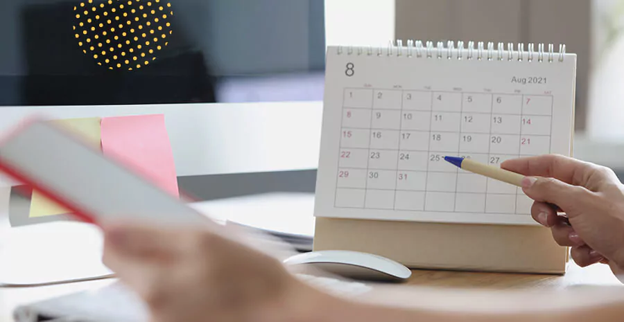 imagem de um calendário em cima de uma mesa com uma pessoa segurando uma caneta na frente dele